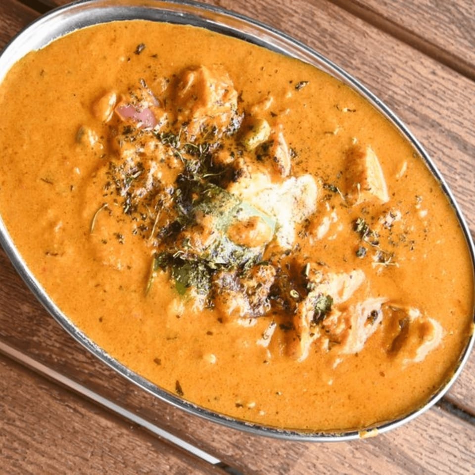 Mirchi Indian Cuisine's creamy orange chicken curry, garnished with herbs, in a silver bowl on wood.