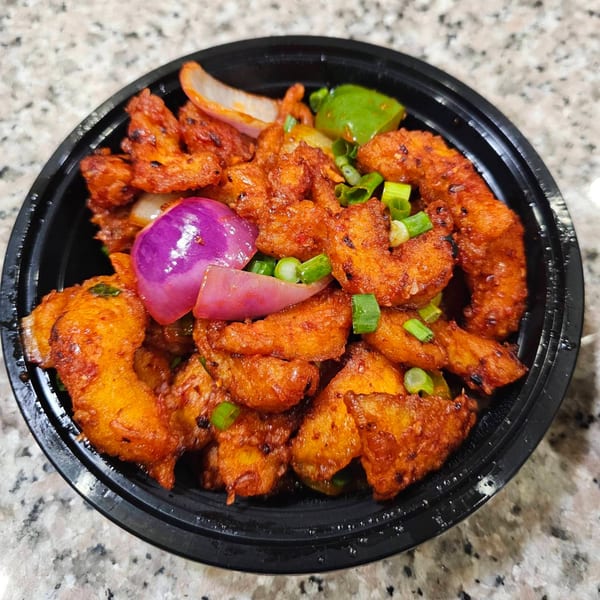 Mirchi Indian Cuisine's chili paneer, with red onions, green peppers, and scallions in a black bowl.