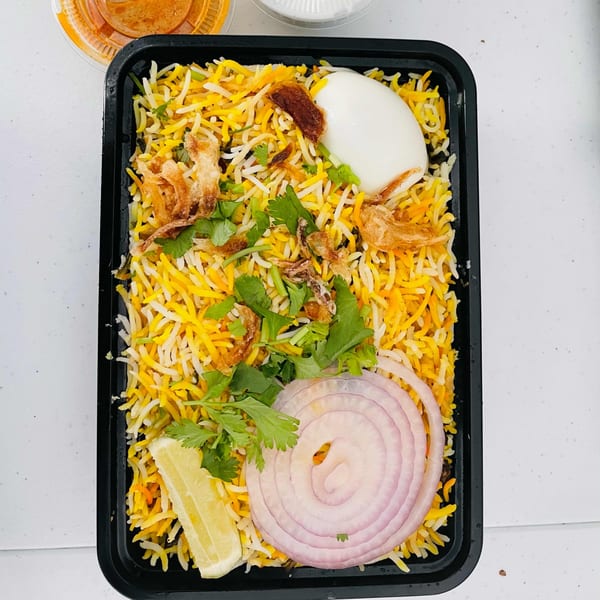 Mirchi Indian Cuisine's egg biryani with rice, cilantro, onions, lemon, and a hard-boiled egg.