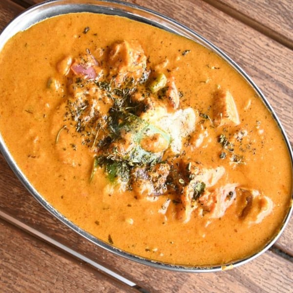 Mirchi Indian Cuisine's creamy orange chicken curry with herbs in a silver bowl on a wooden table.