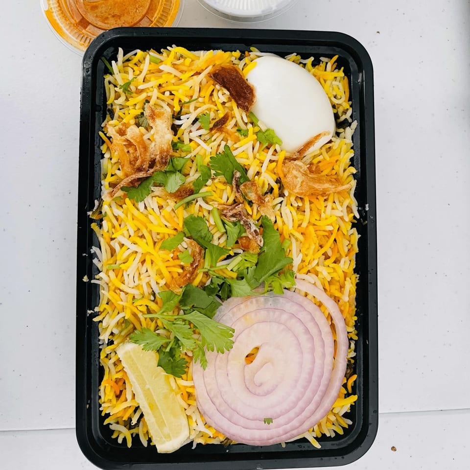 Mirchi Indian Cuisine's biryani with rice, egg, cilantro, fried onions, and a lemon wedge.
