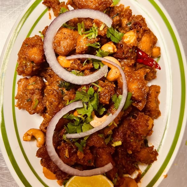 Mirchi Indian Cuisine's Chicken 65, garnished with red onion, cashews, cilantro, and a lime wedge.