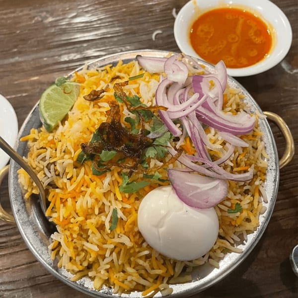 Mirchi Indian Cuisine's biryani with rice, egg, red onions, lime, and a side of red sauce.